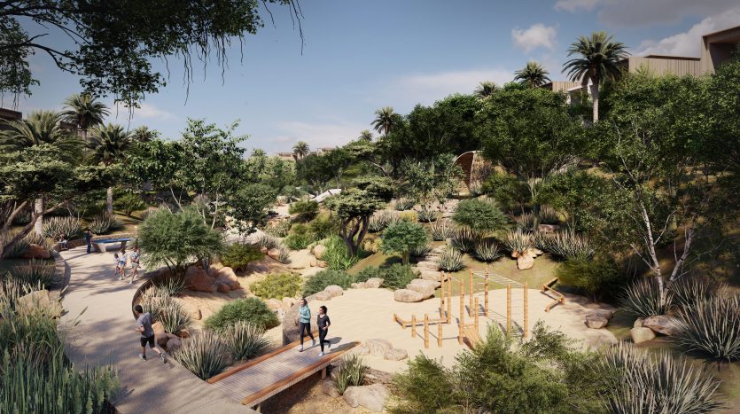 Allée de jardin luxuriante avec des gens marchant et explorant, entourée de diverses plantes, rochers et structures en bois sous un ciel clair à Dubaï.