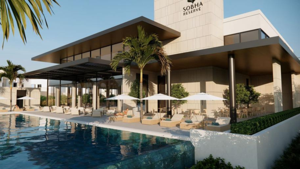 Espace luxueux au bord de la piscine de la réserve Sobha à Dubaï, comprenant des chaises longues sous des parasols, des plantes paysagères et une piscine bleu clair reflétant le ciel.