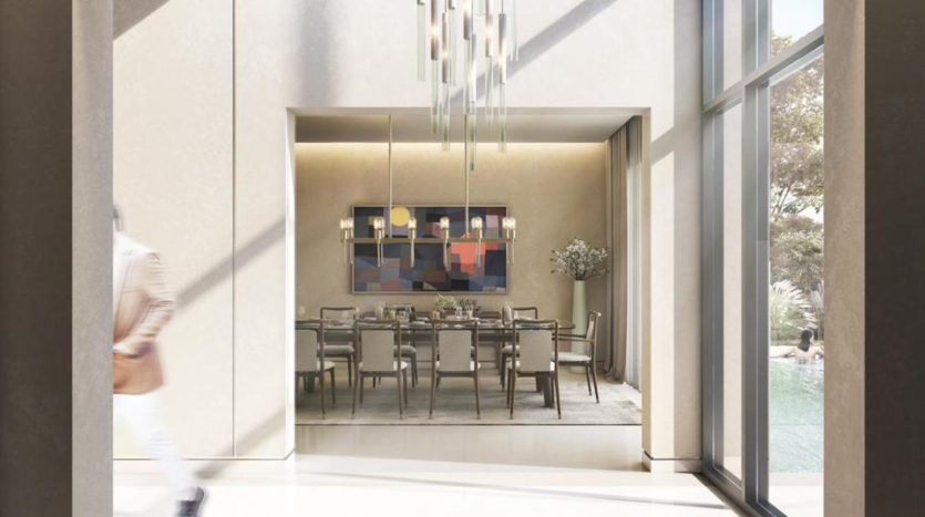 Une salle à manger moderne dans une villa de Dubaï avec une grande table et des chaises, une peinture abstraite colorée au mur et de grandes fenêtres donnant sur une piscine. Une personne passe devant la porte dans le flou,