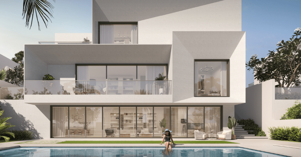 Une villa blanche moderne à plusieurs niveaux avec de grandes fenêtres, des balcons et une piscine. Une personne se promène au bord de la piscine entourée d’une verdure luxuriante. Cette propriété est répertoriée par un top AG