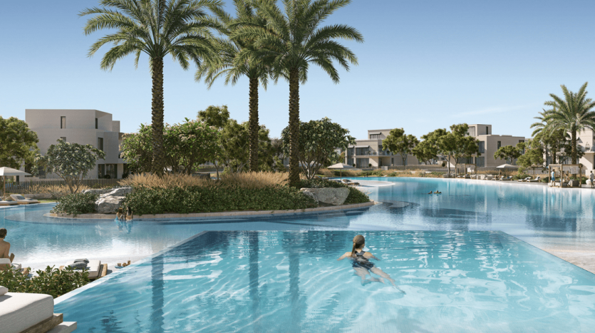 Une piscine luxueuse entourée de palmiers, où les gens se détendent et nagent sous un ciel bleu clair. À proximité, des villas modernes ajoutent au cadre serein, mettant en valeur le premier immobilier de Dubaï.