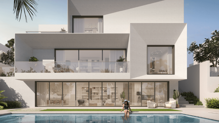 Villa moderne de trois étages à Dubaï avec de grandes fenêtres en verre, des balcons spacieux et une piscine rectangulaire devant. Une personne est assise au bord de la piscine dans une pose détendue. Verdure luxuriante