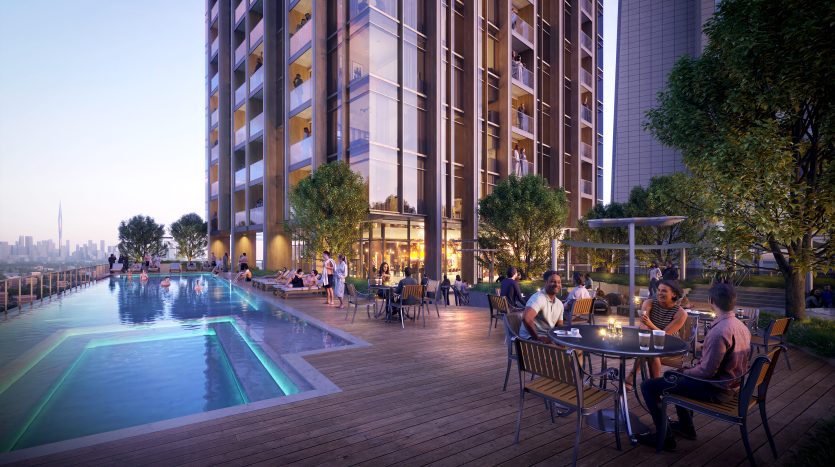Les gens dînent et socialisent sur une terrasse éclairée au bord d&#039;une piscine à débordement dans un appartement moderne de grande hauteur à Dubaï en soirée, avec un horizon de la ville en arrière-plan.