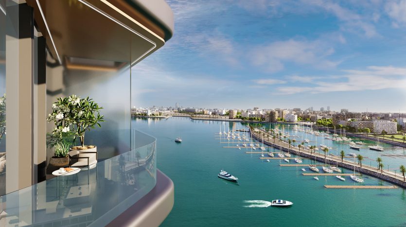 Une vue panoramique depuis un balcon en hauteur surplombant une rivière animée de bateaux. Une silhouette de ville remplit l’horizon sous un ciel clair. Des plantes en pot décorent le balcon de l&#039;appartement Dubaï.