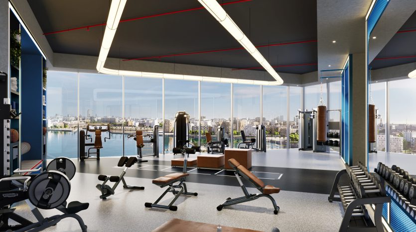 Un intérieur de salle de sport moderne avec de grandes fenêtres offrant une vue sur la ville de Dubaï, comprenant divers équipements d&#039;entraînement, des bancs et un éclairage zénithal dans un cadre spacieux.
