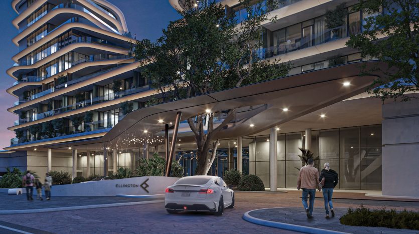 Entrée d&#039;un bâtiment de luxe moderne au crépuscule avec un design incurvé et un auvent éclairé, avec une voiture de sport blanche et des passants à Dubaï.