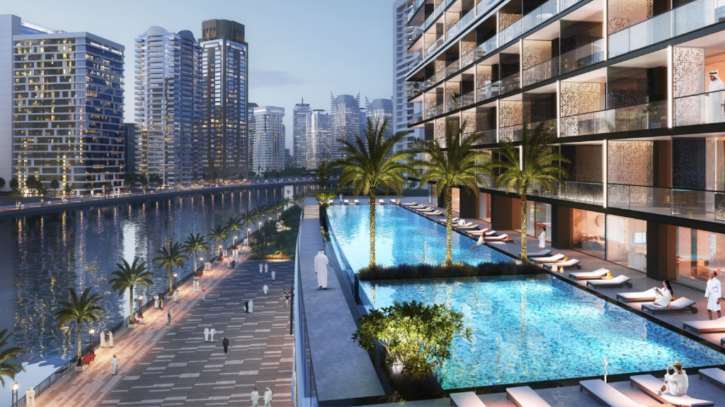 Luxueuse promenade urbaine en bord de mer à Dubaï, flanquée d&#039;immeubles modernes de grande hauteur, comprenant une piscine illuminée en bleu, des sentiers pédestres et des chaises longues dispersées.