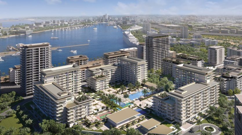 Vue aérienne d&#039;un quartier résidentiel moderne en bord de mer avec plusieurs immeubles de grande hauteur, des espaces verts luxuriants et une marina animée avec des bateaux, le tout surplombant les toits de la ville et la rivière de Dubaï.