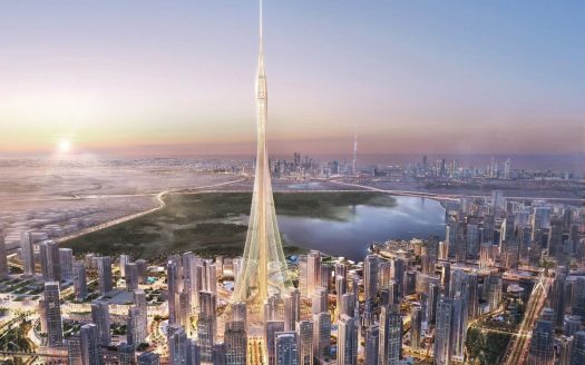 Vue aérienne d'une ville futuriste au coucher du soleil avec un gratte-ciel imposant et élancé au centre, entouré de nombreux immeubles de grande hauteur, dont plusieurs propriétés de l'immobilier Dubaï et un grand plan d'eau.