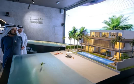 Deux hommes examinent un modèle architectural détaillé d&#039;un immeuble résidentiel moderne et du paysage environnant à Dubaï, exposé sous un éclairage intense dans une pièce avec la marque de l&#039;entreprise sur le mur du fond.