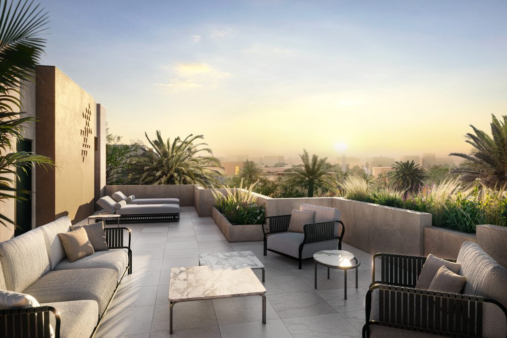 Luxueux toit-terrasse au coucher du soleil avec mobilier d&#039;extérieur moderne, plantes en pot luxuriantes et vue panoramique sur les toits de Dubaï partiellement obscurcis par la verdure.