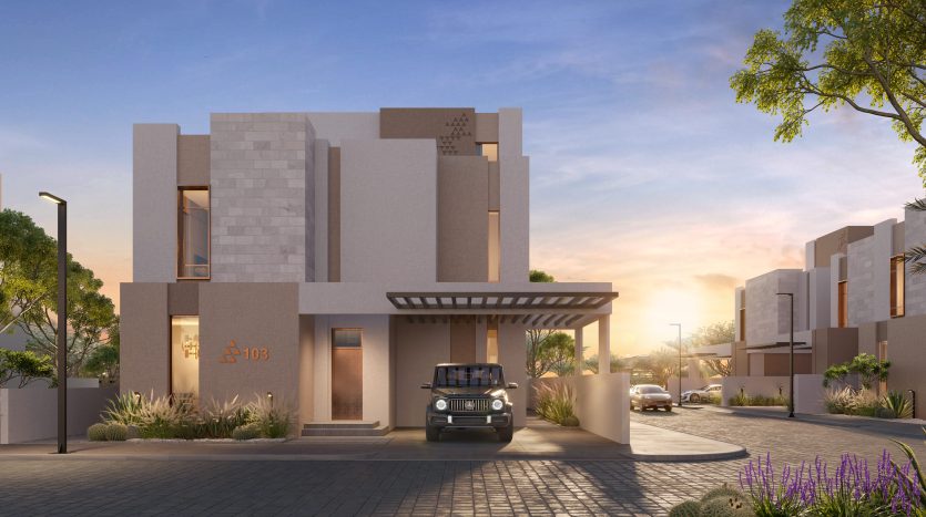 Une maison moderne avec un toit plat et une façade beige au coucher du soleil, située dans le quartier immobilier privilégié de Dubaï. Une voiture est garée sous l&#039;allée couverte. Un aménagement paysager bien entretenu met en valeur