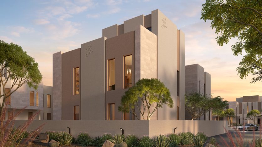 Bâtiment résidentiel moderne au design minimaliste avec des tons neutres, de grandes fenêtres et entouré d&#039;un aménagement paysager désertique avec de petits arbres et arbustes sous un ciel coucher de soleil. Idéal comme opportunité d’investissement à Dubaï.