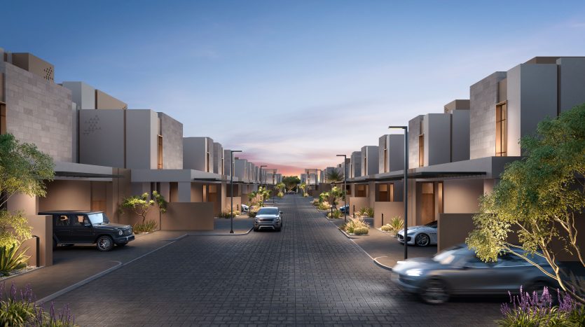 Rue résidentielle moderne au crépuscule avec des maisons symétriques, des voitures dans les allées et un ciel rose et bleu vif. Les arbres décoratifs et l&#039;aménagement paysager rehaussent l&#039;atmosphère tranquille de la banlieue, qui rappelle un quartier chic de Dubaï.