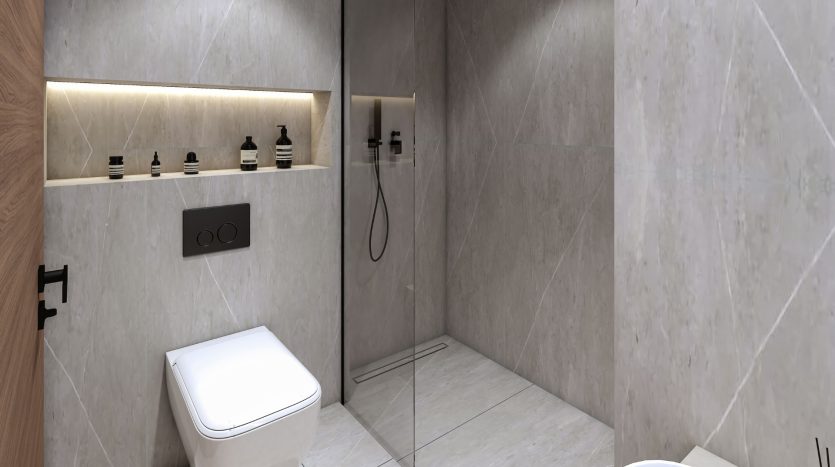 Salle de bains moderne et minimaliste avec murs en marbre gris clair, toilettes murales et espace douche en verre avec pomme de douche à main noire. Un éclairage chaleureux met en valeur le coin vanité, parfait pour un investissement à Dubaï