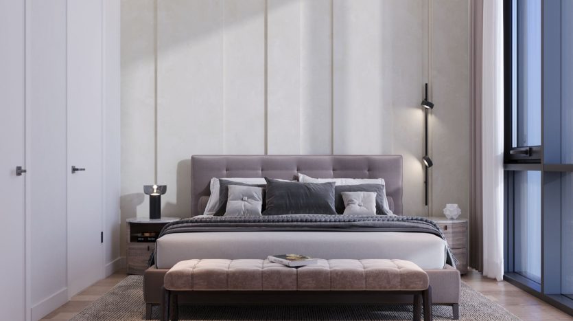 Une chambre moderne dans un appartement de Dubaï comprenant un grand lit avec une literie grise et noire, flanqué d'une table de nuit avec une lampe et un banc au pied du lit. La lumière d'un