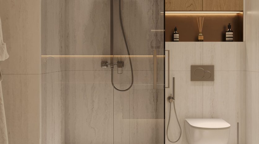 Salle de bains moderne dans un appartement de Dubaï comprenant une cloison de douche en verre, un miroir lumineux, des carreaux beiges chauds et des toilettes blanches. Il ajoute une touche d&#039;élégance avec une décoration minimaliste et un éclairage tamisé.