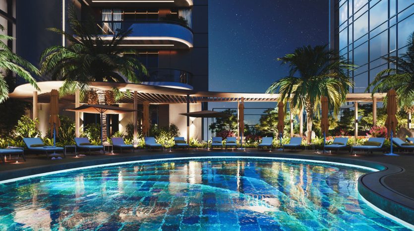 Piscine luxueuse du complexe la nuit avec éclairage ambiant, entourée de chaises longues et de verdure luxuriante, adjacente aux façades de bâtiments modernes sous un ciel étoilé, parfaite pour un investissement immobilier à Dubaï.