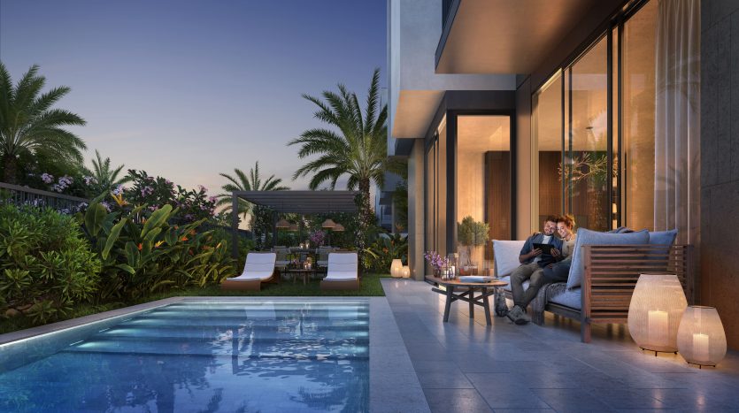Un couple profite d’une soirée sereine sur la terrasse au bord de la piscine de leur villa à Dubaï, entouré d’une verdure luxuriante et d’un mobilier d’extérieur moderne sous un ciel crépusculaire.