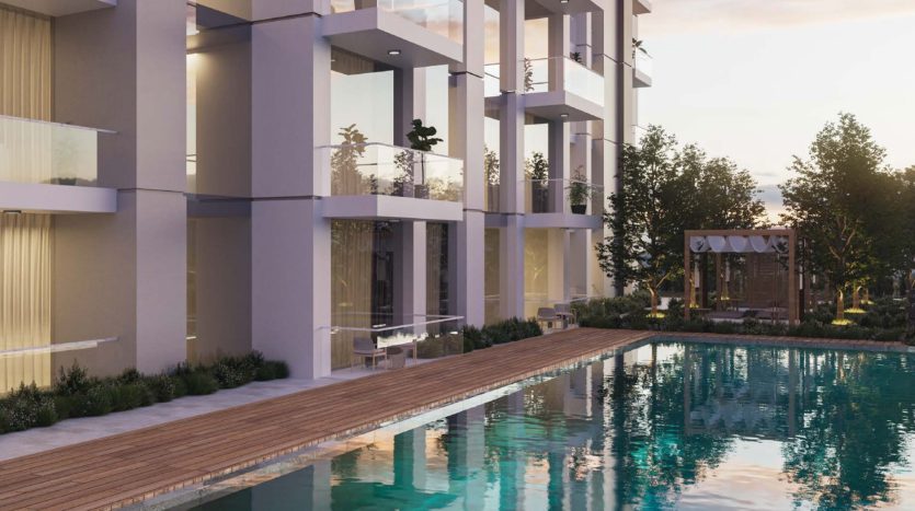 Immeuble résidentiel moderne avec balcons en verre donnant sur une piscine tranquille entourée d&#039;une terrasse en bois au coucher du soleil, parfait pour ceux qui explorent le marché immobilier de Dubaï.