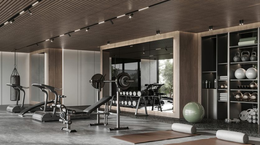 Salle de sport moderne à domicile avec divers équipements d&#039;exercice, notamment des tapis roulants, des poids et un vélo, avec des touches de bois et de grandes fenêtres en verre dans un appartement de Dubaï.