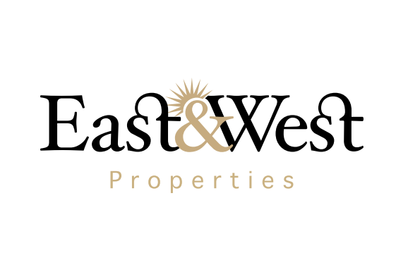 Logo de &quot;east&amp;west Properties&quot; comportant un texte stylisé avec un motif de soleil au-dessus de l&#039;esperluette, représentant une agence immobilière Dubaï, dans un jeu de couleurs noir et or.