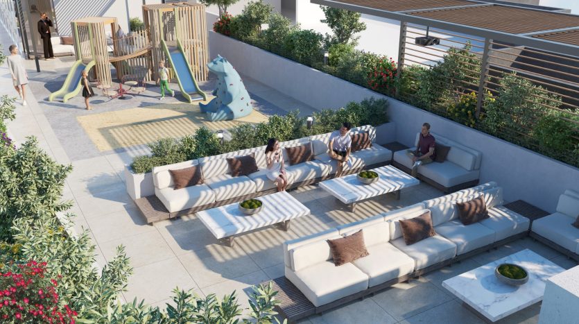 Un toit-terrasse à Dubaï comprenant des coins salons blancs intégrés avec des coussins marron, de petites plantes vertes sur les tables et une structure de jeu en bois pour enfants en arrière-plan. Les gens sont dispersés, assis et parlent ou