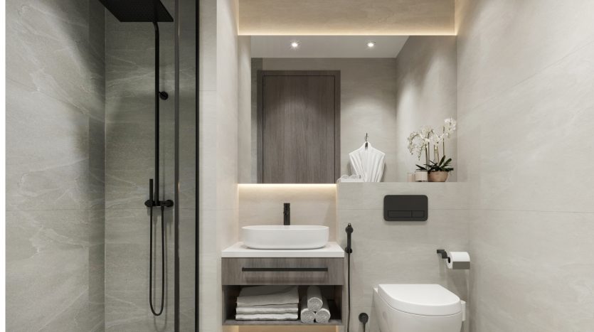 Intérieur de salle de bains moderne comprenant un meuble en bois avec un lavabo blanc, un miroir, des toilettes murales et une douche à l&#039;italienne dans un appartement de Dubaï, accentué par des carreaux de pierre grise et un éclairage chaleureux