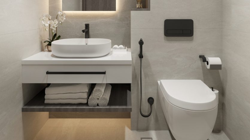 Une salle de bains moderne dans une villa de Dubaï comprenant un lavabo blanc sur une vanité flottante avec des tiroirs, des toilettes murales et des luminaires noirs, le tout sur des murs carrelés neutres.