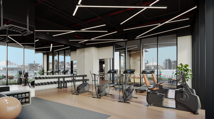 Intérieur de salle de sport moderne avec tapis roulants, vélos stationnaires et espace de musculation. La salle de sport dispose de grandes fenêtres avec vue sur Dubaï et d&#039;un élégant éclairage rouge au plafond.