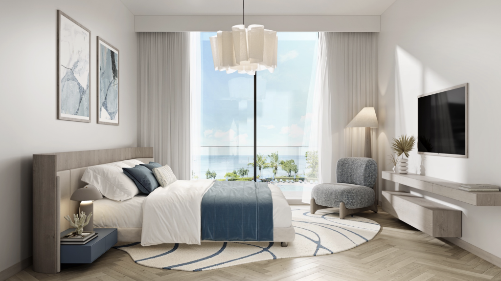 Chambre moderne dans un appartement de Dubaï comprenant un grand lit recouvert d&#039;une literie bleue, une tête de lit en bois, une baie vitrée offrant une vue sur l&#039;océan et une décoration minimaliste comprenant une télévision murale et des œuvres d&#039;art.