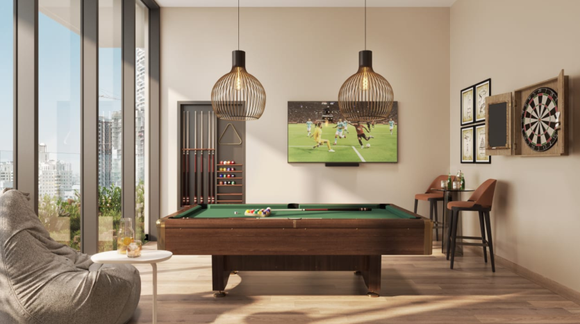 Un salon moderne avec une table de billard, un jeu de fléchettes, des suspensions et une grande télévision diffusant un match de football. Les baies vitrées offrent une vue impressionnante sur la ville de Dubaï.
