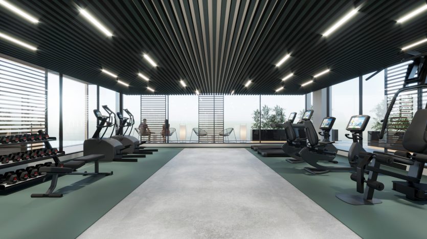 Une salle de sport moderne avec machines cardio et poids donnant sur une baie vitrée, sous un plafond aux lumières linéaires. L&#039;espace est propre, lumineux et bien équipé pour les entraînements, parfait pour les investisseurs axés sur l&#039;immobilier