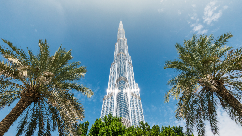 Une vue saisissante sur le Burj Khalifa encadré par deux palmiers sous un ciel bleu clair, mettant en valeur les offres époustouflantes de l&#039;immobilier Dubaï. La lumière du soleil se reflète sur la surface métallique élégante du bâtiment.