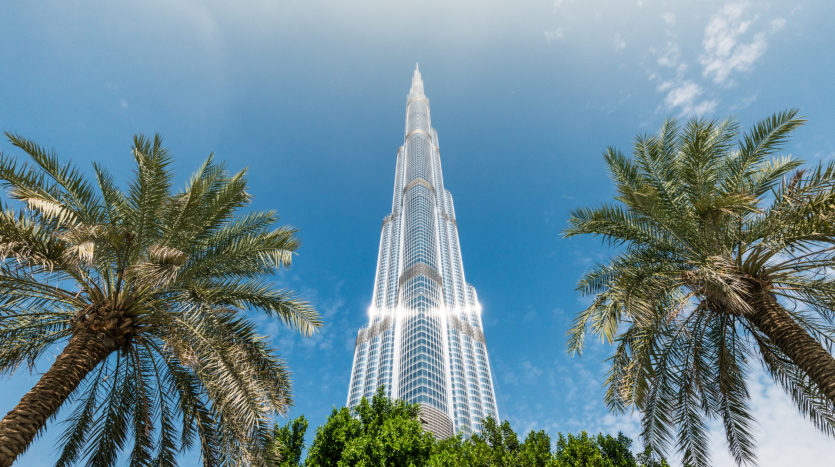 Une vue saisissante sur le Burj Khalifa encadré par deux palmiers sous un ciel bleu clair, mettant en valeur les offres époustouflantes de l&#039;immobilier Dubaï. La lumière du soleil se reflète sur la surface métallique élégante du bâtiment.