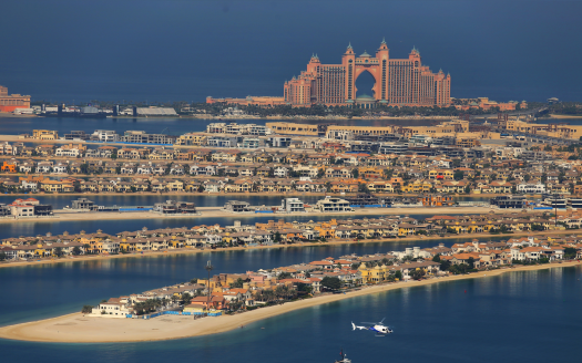 Vue aérienne d'une ville côtière présentant l'emblématique hôtel Atlantis sur Palm Jumeirah à Dubaï, entouré de résidences luxueuses et d'une mer limpide, avec un hélicoptère volant à proximité.