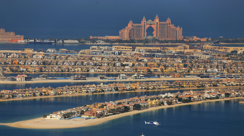 Vue aérienne d&#039;une ville côtière présentant l&#039;emblématique hôtel Atlantis sur Palm Jumeirah à Dubaï, entouré de résidences luxueuses et d&#039;une mer limpide, avec un hélicoptère volant à proximité.