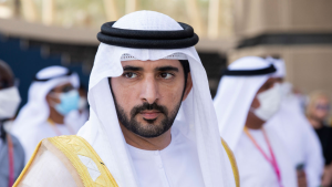 Un homme vêtu d&#039;une tenue traditionnelle émiratie, comprenant une kandura blanche et une ghutra noire et blanche, regarde pensivement devant lui un événement en plein air près d&#039;une villa à Dubaï.