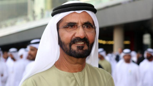 Un homme vêtu d'une tenue traditionnelle émiratie, comprenant un kandura blanc et un agal noir, se tient dans un quartier de villas bondé à Dubaï, souriant légèrement à la caméra.