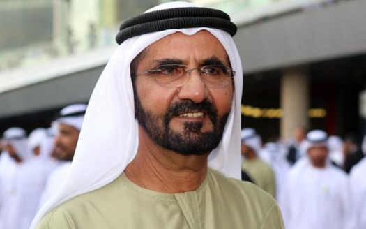 Ein Mann in traditioneller emiratischer Kleidung, die aus einer weißen Kandura und einem schwarzen Agal besteht, steht in einem überfüllten Villenviertel in Dubai und lächelt leicht in die Kamera.
