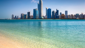 Ein Panoramablick über die Dächer einer modernen Stadt mit großen Wolkenkratzern, die sich in einem ruhigen, türkisfarbenen Meer unter einem klaren blauen Himmel spiegeln - perfekt für diejenigen, die über einen Immobilienmakler in Dubai Immobilienoptionen erkunden.