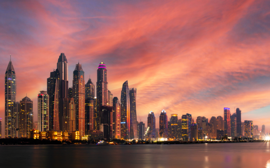 Une ligne d&#039;horizon à couper le souffle de Dubaï avec de nombreux gratte-ciels illuminés sous un ciel coucher de soleil vibrant avec des nuages tourbillonnants roses et oranges.