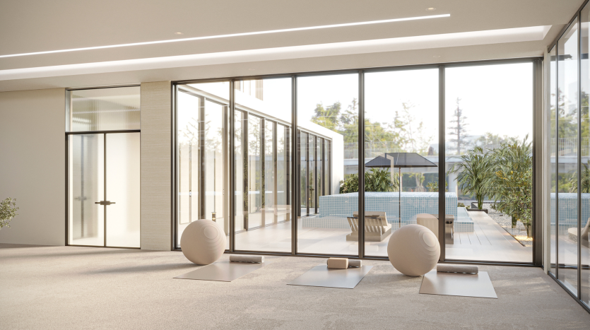 Un studio de yoga moderne et spacieux avec de grands murs de verre donnant sur une piscine sereine dans une villa de Dubaï, comprenant deux ballons d'exercice et des tapis de yoga sur un sol élégant, entouré de lumière naturelle.