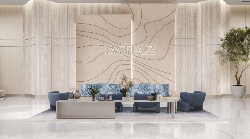 Un hall d'entrée moderne et luxueux doté d'un grand mur beige avec des motifs abstraits et le texte « IMTIAZ ». L'espace comprend des chaises rembourrées bleues, une longue table basse grise avec des objets décoratifs, un sol en marbre et des plantes en pot renforçant l'ambiance élégante, parfaite pour une atmosphère inspirée d'une promenade sur la plage.