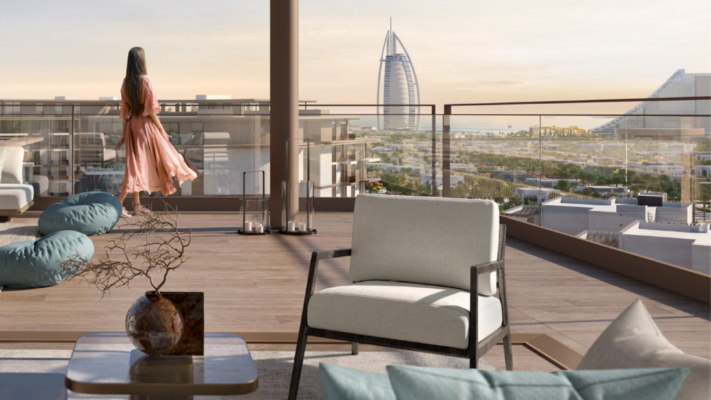 Une femme vêtue d'une robe fluide se tient sur le balcon spacieux d'un appartement luxueux à Dubaï, surplombant un paysage urbain avec des gratte-ciel emblématiques, à côté de meubles de patio élégants et d'éléments décoratifs.