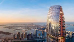 Vue aérienne d'un gratte-ciel moderne avec une façade en verre incurvée au coucher du soleil, surplombant un paysage urbain côtier avec des routes bien aménagées et d'autres immeubles de grande hauteur à Dubaï.