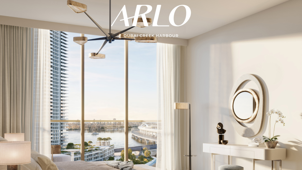 Une chambre sereine et moderne avec des baies vitrées donnant sur le front de mer du port de Dubai Creek près d&#039;Emaar. La pièce dispose d&#039;un lustre chic, d&#039;un élégant miroir circulaire au-dessus d&#039;une console blanche et d&#039;un décor minimaliste pour une atmosphère tranquille. &quot;ARLO&quot; est écrit en haut.