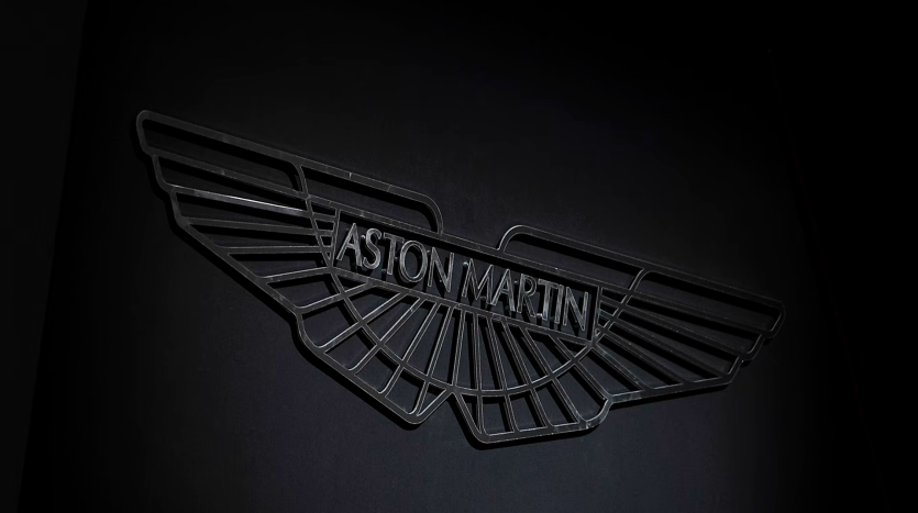 Image en gros plan d'un élégant logo Aston Martin noir représenté avec des ailes stylisées et le nom de la marque en relief au centre sur un fond sombre.