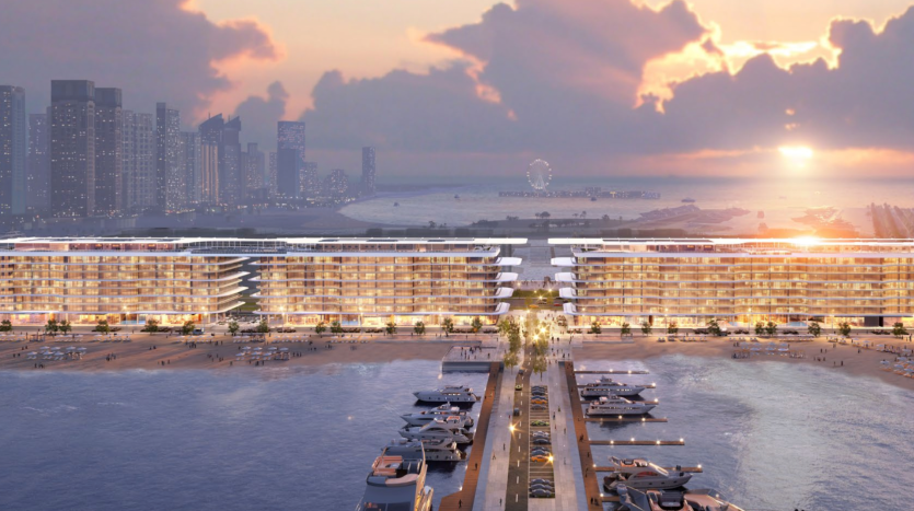 Un superbe développement en bord de mer au coucher du soleil comprenant les Dubai Harbour Residences, avec deux bâtiments modernes de plusieurs étages dotés de balcons spacieux donnant sur une marina remplie de yachts. Le paysage urbain et les grands gratte-ciel forment la toile de fond, avec une grande roue visible au loin sous un ciel coloré.