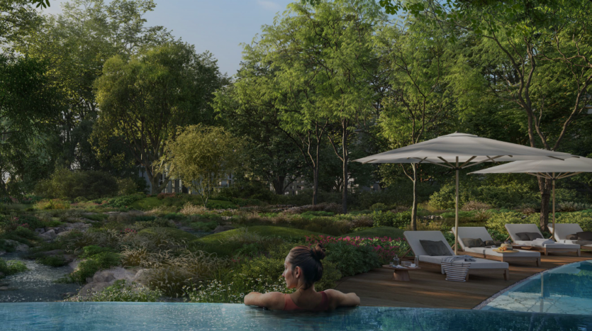 Une femme se détend dans une luxueuse piscine à débordement donnant sur un jardin luxuriant et verdoyant avec des arbres et diverses plantes. A proximité, il y a des chaises longues sous des parasols blancs sur une terrasse en bois, créant un cadre extérieur serein et paisible rappelant les bois tranquilles de ghaf.